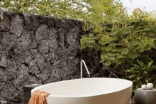 20 a peaceful space with a stone wall for privacy, a concrete table and an oval free-standing bathtub