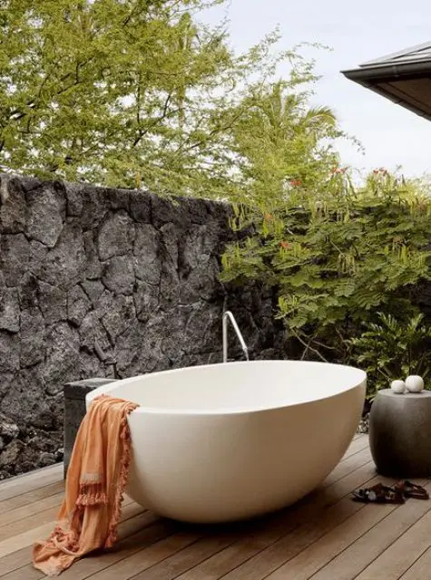 a peaceful space with a stone wall for privacy, a concrete table and an oval free-standing bathtub