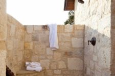 22 a cozy outdoor rustic shower fully clad with stone, with a little built-in storage item and a chair