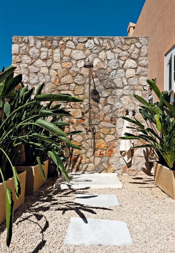 a lovely outdoor shower with a stone wall, pebble and stone floor and potted plants