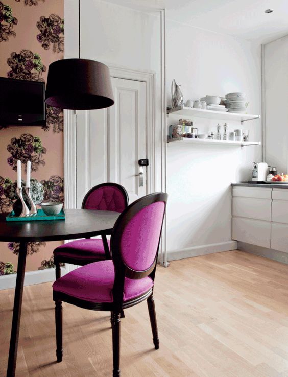 a chic dining space with elegant magenta chairs and floral wallpaper to separate it from the kitchen