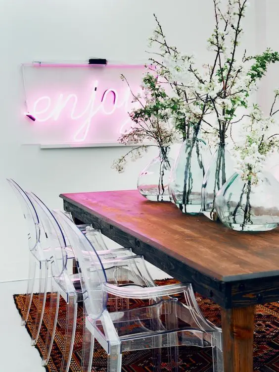 a modern dining space done with a pink neon light and acrylich chairs that contrast the wooden table