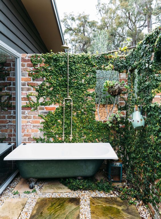 A vintage industrial outdoor space with a brick wall covered with winves and a green bathtub