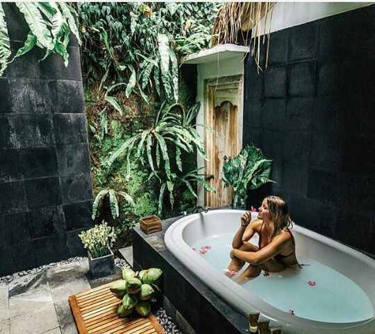 an outdoor sanctuary with a tile clad bathtub, pebbles and a wooden mat plus potted plants
