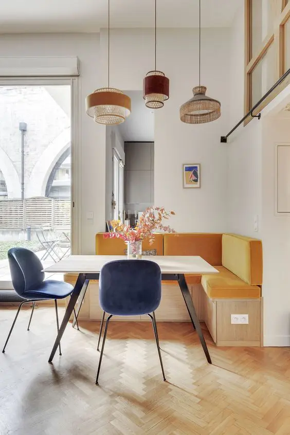 a bold modern dining nook with a yellow banquette seating, a stable and blue chairs, a cluster of pendant lamps