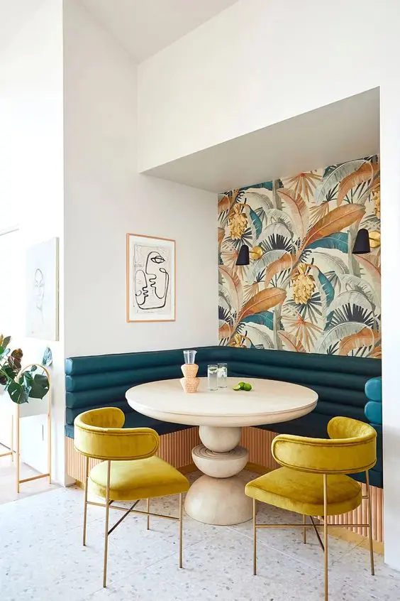 a bright and elegant dining nook with an accent wall, a stained table, yellow chairs and a navy banquette seating