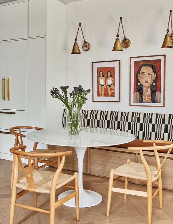 a bright dining nook with a banquette seating, a round table, woven chairs, a gallery wall and brass sconces