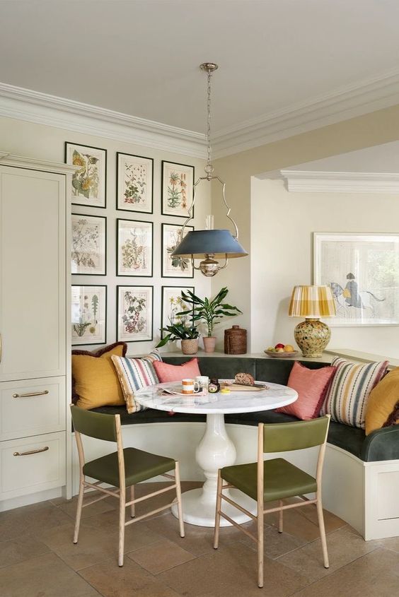 a chic and refined dining room with a banquette seating, a round table, green chairs, a pendant lamp and a gallery wall of vintage posters
