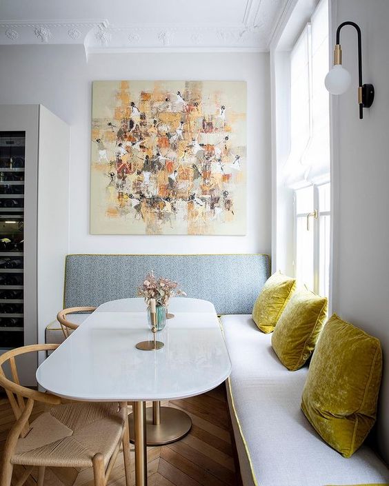 a chic modern dining nook with a banquette seating, a table and woven chairs, an oversized artwork