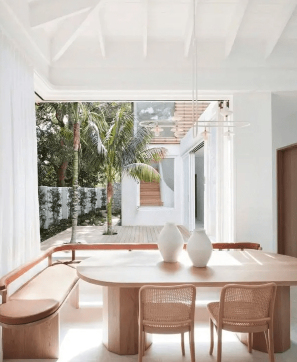 A contemporary tropical indoor outdoor eating space with a leather and wood banquette seating, a curved table and woven chairs by the terrace entrance