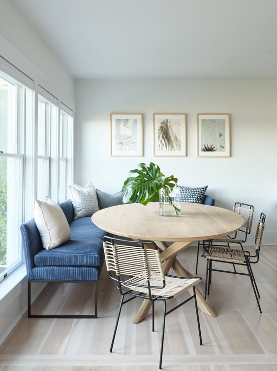 a dreamy coastal dining room with a blue banquette seating, a round table, woven chairs and a gallery wall
