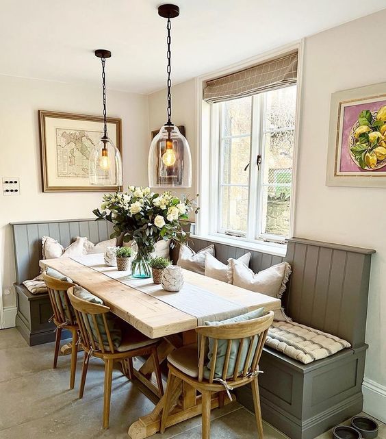 a farmhouse dining room with a grey banquette seating, a stained trestle table, stained chairs, pendant lamps and some decor