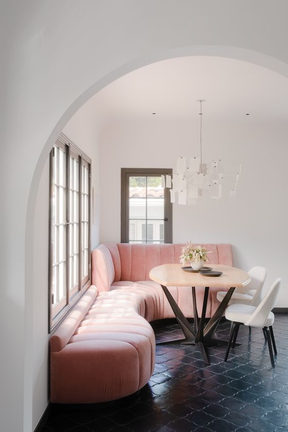 a glam dining room with a pink upholstered banquette seating, a table and white chairs and a chandelier