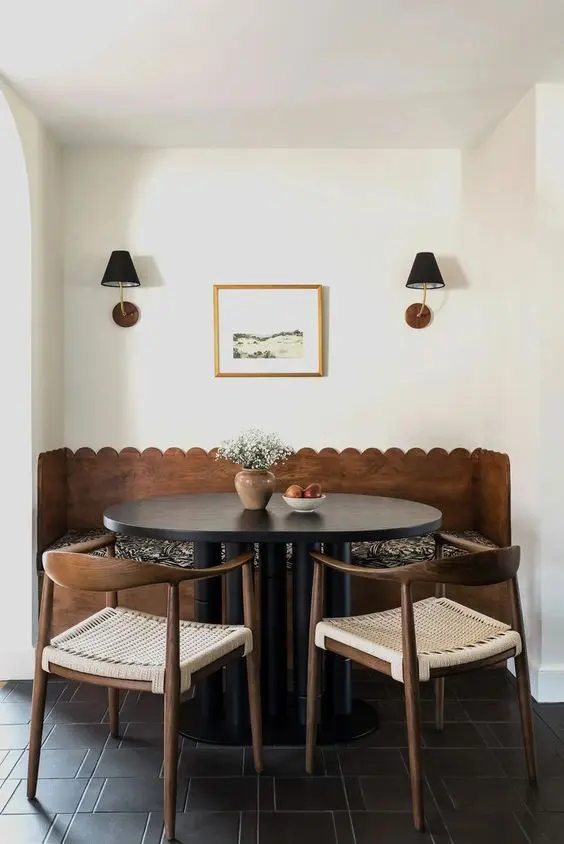 a mid-century modern dining space with a built-in banquette seating with a scallop edge, a black table and woven chairs, black wall lamps