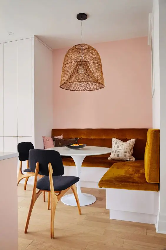 a modern and bright dining nook with a rust banquette seating, a white table,graphite grey chairs, a woven pendant lamp