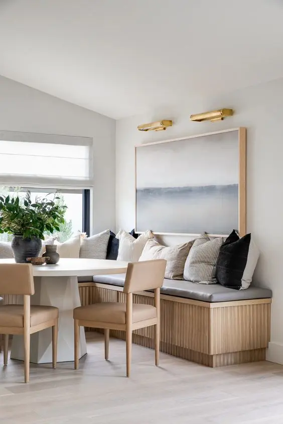 a modern coastal banquette seating with a white table, stained chairs, lots of pillows and a large painting