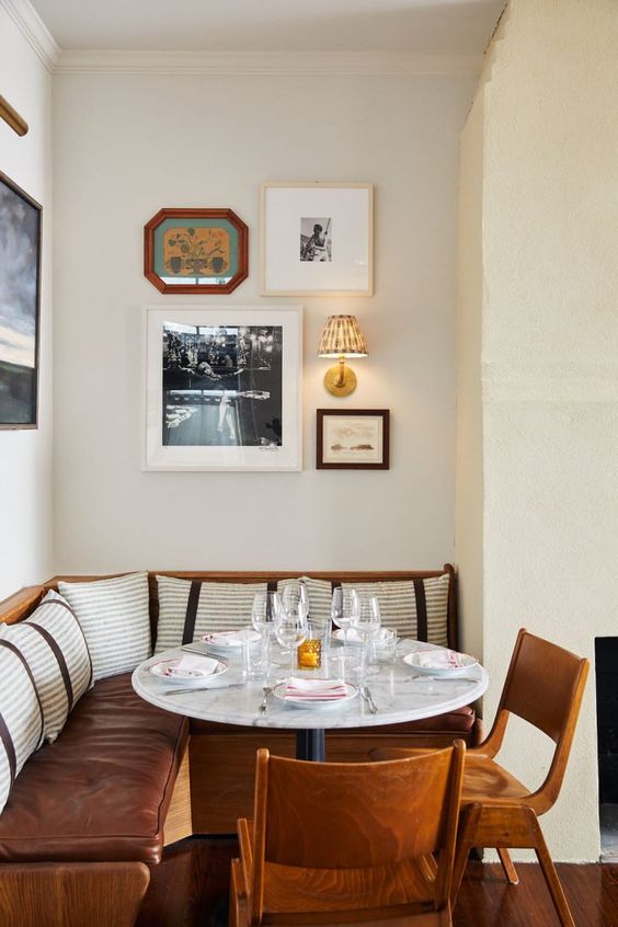 a modern dining nook with a leather banquette seating, a table and stained chairs, a gallery wall is very chic and cozy
