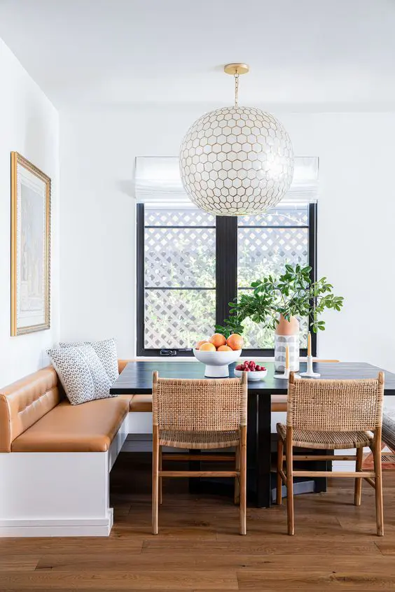 a modern dining room with a banquette seating, a black table, woven chairs and an oversized pendant lamp