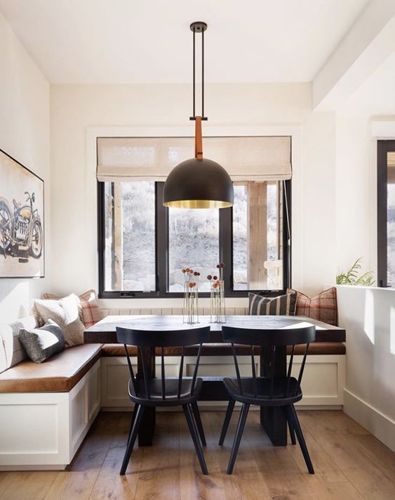 a modern farmhouse dining room with a banquette seating, black chairs, a pendant lamp and some chic decor