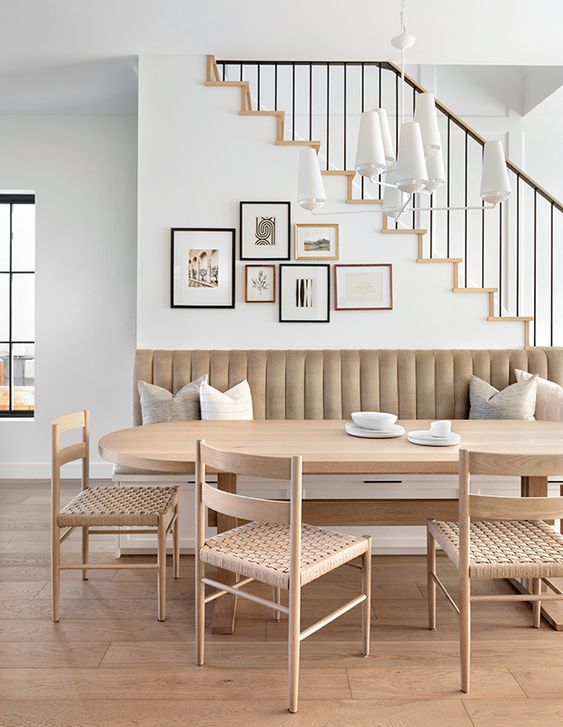 a neutral dining space with a storage banquette seating, an oval table, woven chairs, a gallery wall and a white chandelier