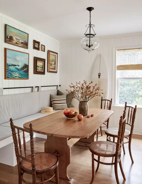 a neutral farmhouse dining space wiht a neutral banquette seating, a vintage stained table and chairs, a gallery wall and a pendant lamp