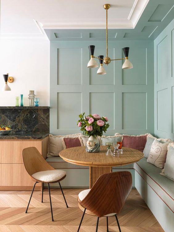 a refined and elegant dining nookw ith aqua walls, a stained table,a  built-in banquette seating, stained chairs and a chic chandelier
