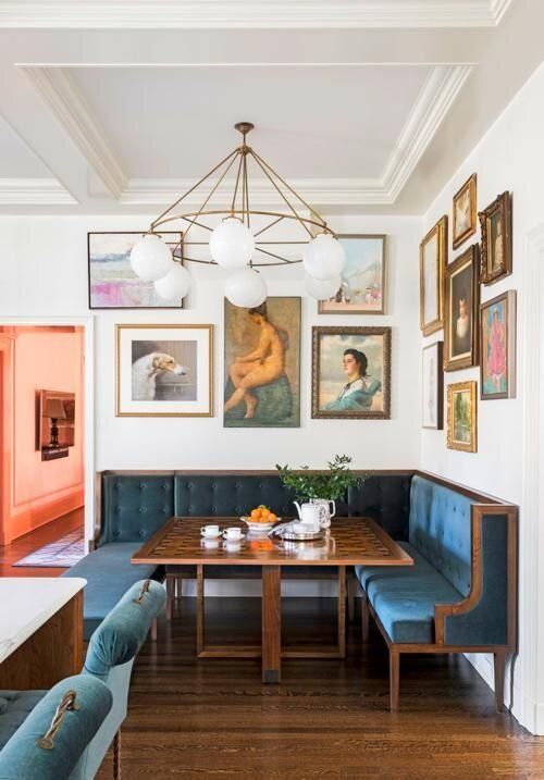 a refined vintage dining nook with a blue banquette seating, a stained table, a large gallery wall and a large chandelier