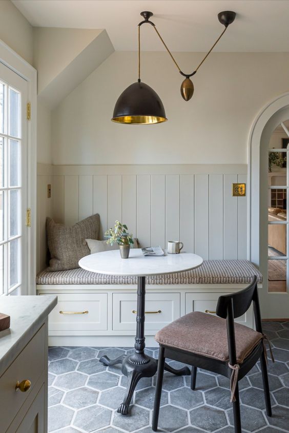 a small and cute dining nook with a storag banquette seating, a small table, a black chair and a black pendant lamp