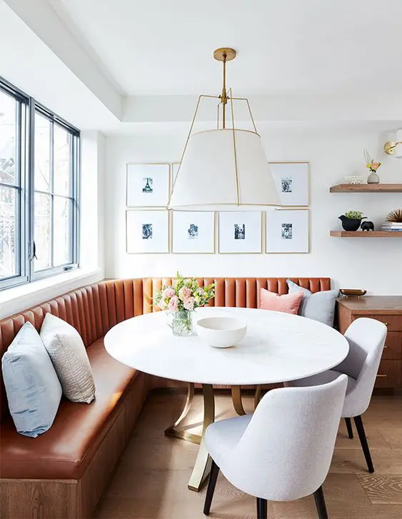 a stylish modern dining room with an orange banquette seating, a white table and neutral chairs, a gallery wlal and some pillows