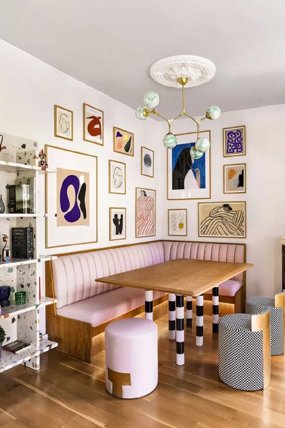 a whimsical and quirky dining space with a pink banquette seating, a table with striped legs and stools, a bold gallery wall