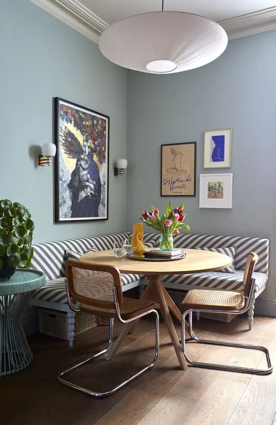 a whimsical dining space with a striped banquette seating, a round table and cane chairs and some bold artwork