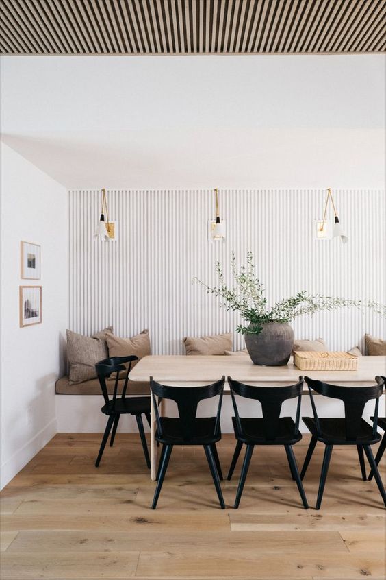 an airy coastal dining room with a striped accent wall, a banquette seating, a table, black chairs, pendant lamps