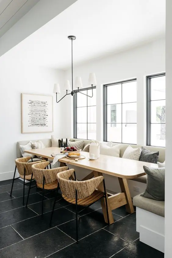 an airy dining room with a banquette seating, a stained table, wood and jute chairs and a chandelier is a cool space