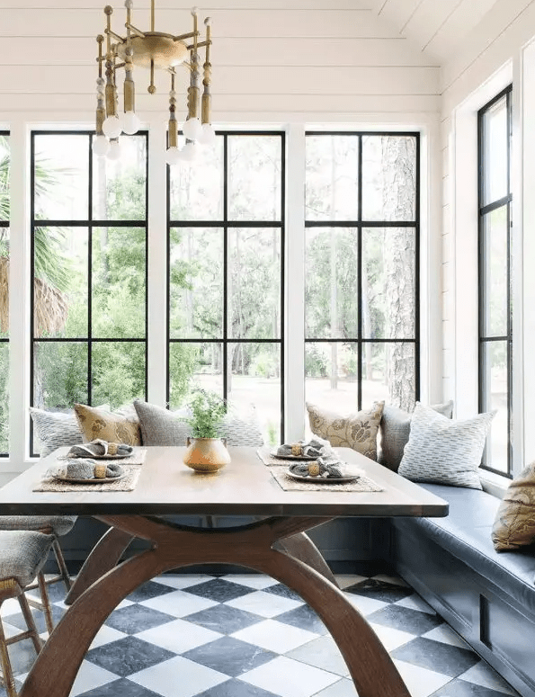 an elegant eating space by a whole gallery of windows, a grey banquette seating, printed pillows, a stained table