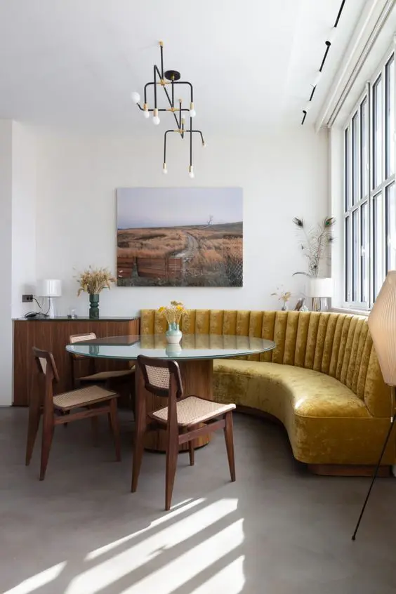 an exquisite dining room with a mustard banquette seating, a glass table, cane chairs, some art and whimsical pendant lamps