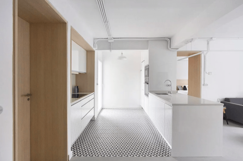 The kitchen is done with sleek white cabinets, a geometric floor and light-colored wood surfaces