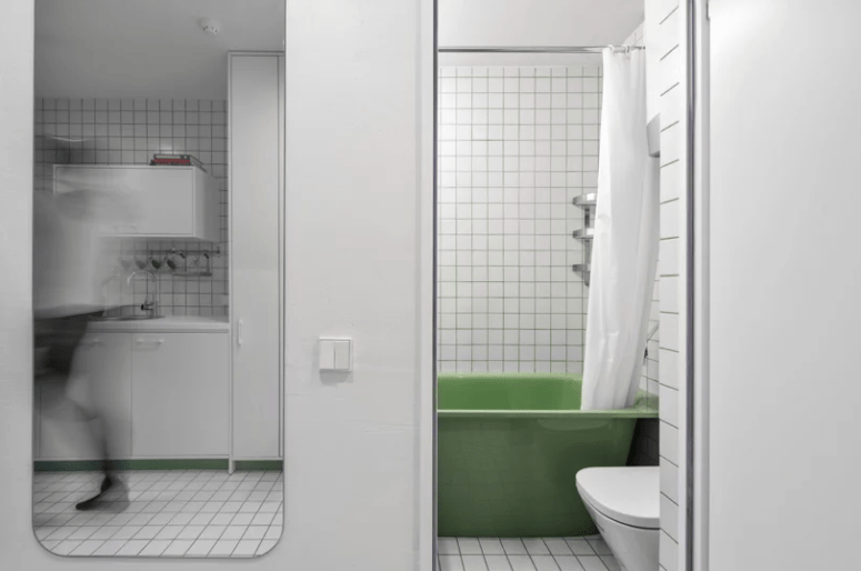 The bathroom is small but still features a comfy green bathtub and even soem shelves