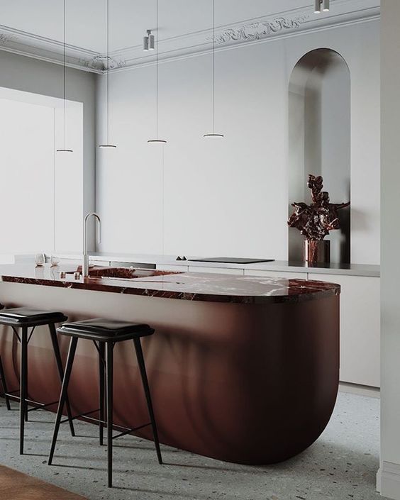 A luxurious modern kitchen with white cabinets and a burgundy colored kitchen island with rounded corners and a marble countertop
