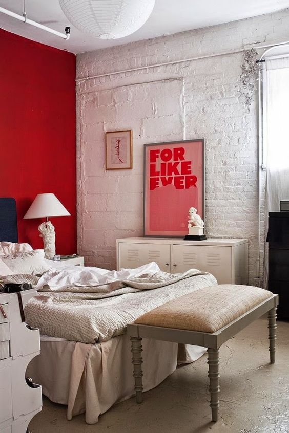 A red accent wall is a bold statement in this white and off white bedroom and an artwork matches