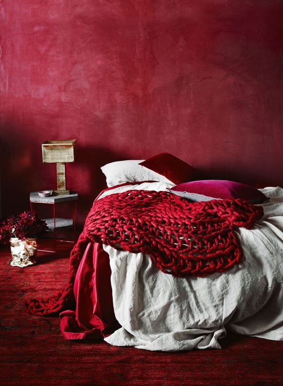 an all-red bedroom with a red wall, carpet, pillows and a chunky knit blanket for a passionate look
