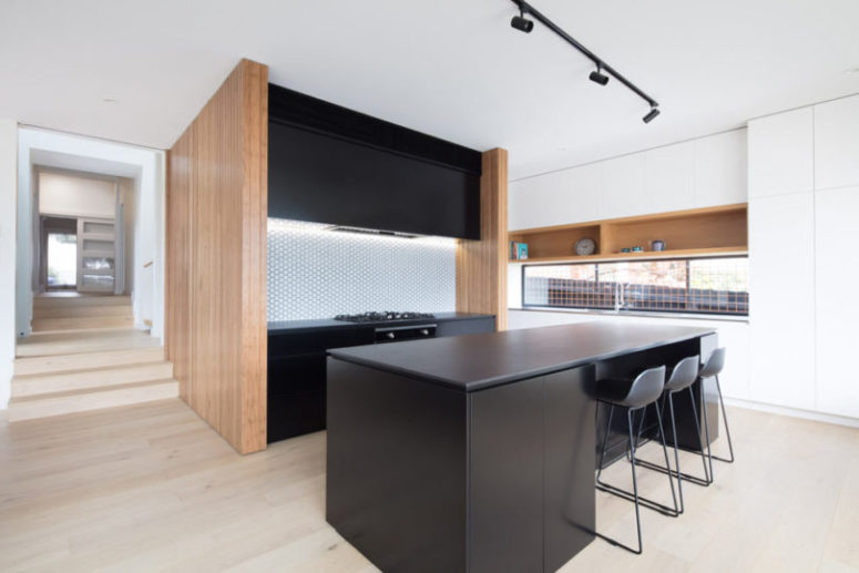 The kitchen is done with black cabinets and light-colored wood, the backsplash is clad with penny tiles