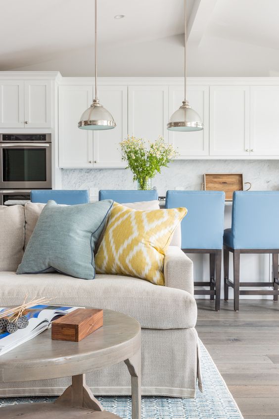a large sofa marks the living space and the blue chairs show off the kitchen