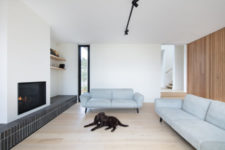 07 The living room is done with light grey sofas, a wood plank wall, a built-in fireplace and some windows