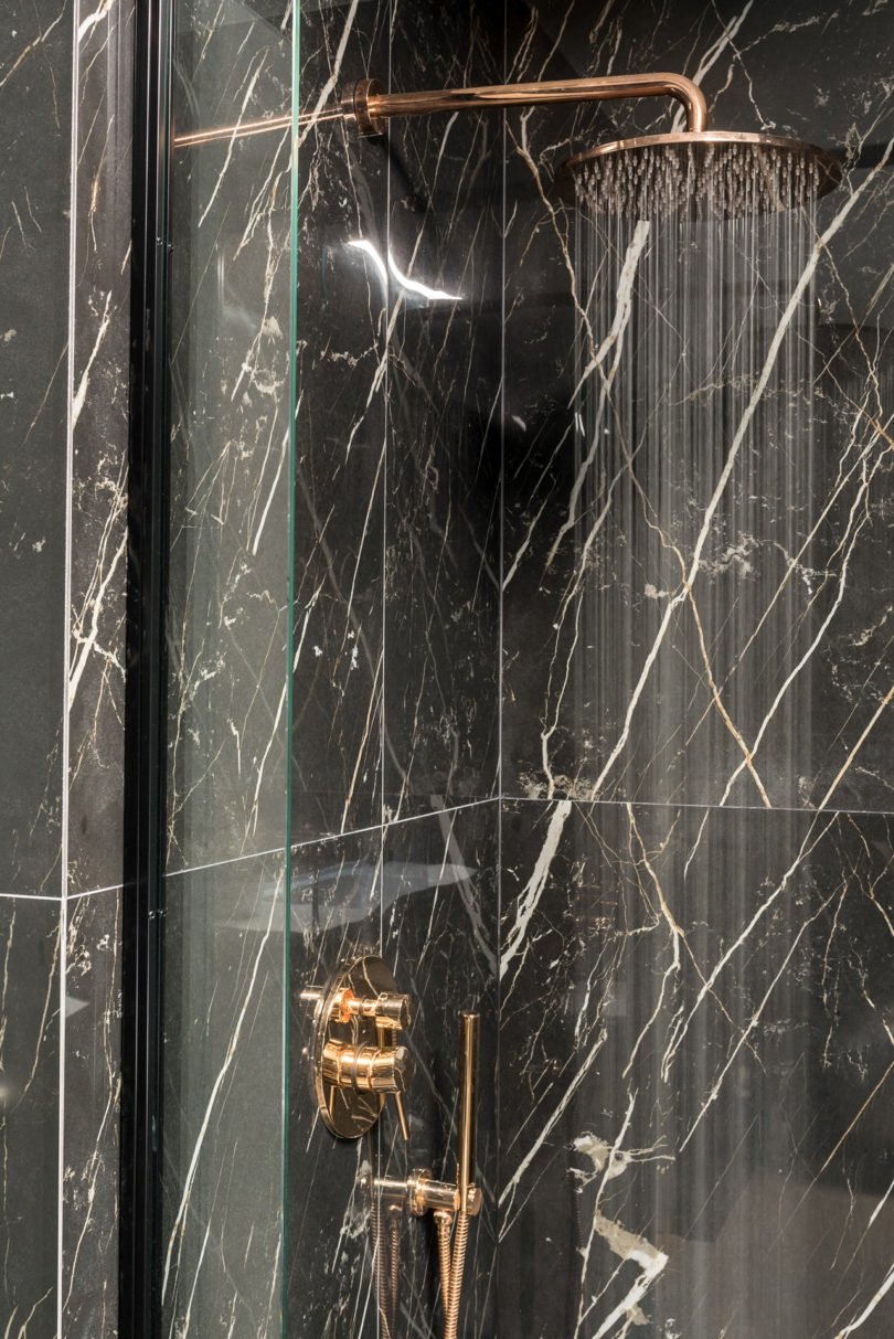 The master bathroom is clad with black marble tiles and is done with edgy copper fixtures