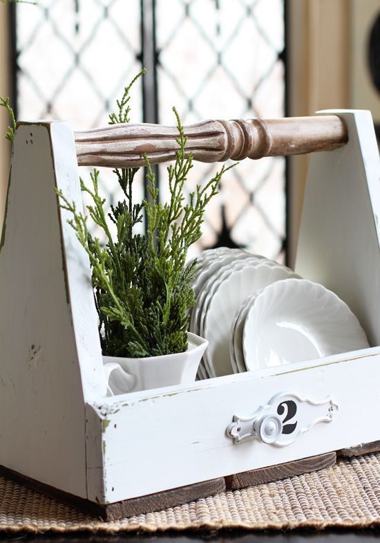 A vintage farmhouse dish caddy of white and stained wood with plates and planted greenery