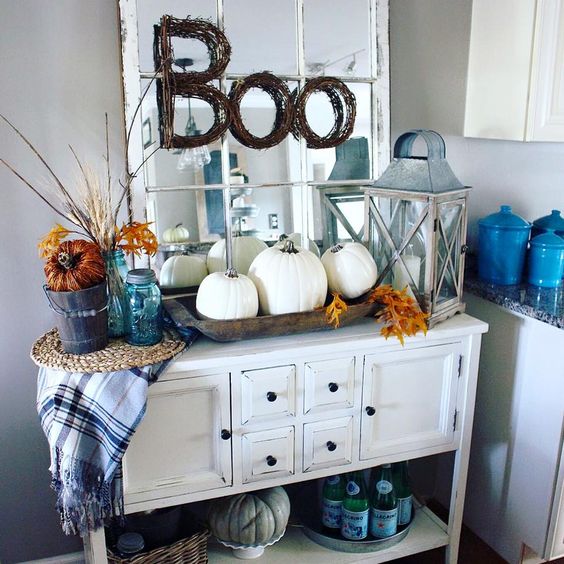 a vintage console with a trio of white pumpkins, fall leaves and a plaid blanket