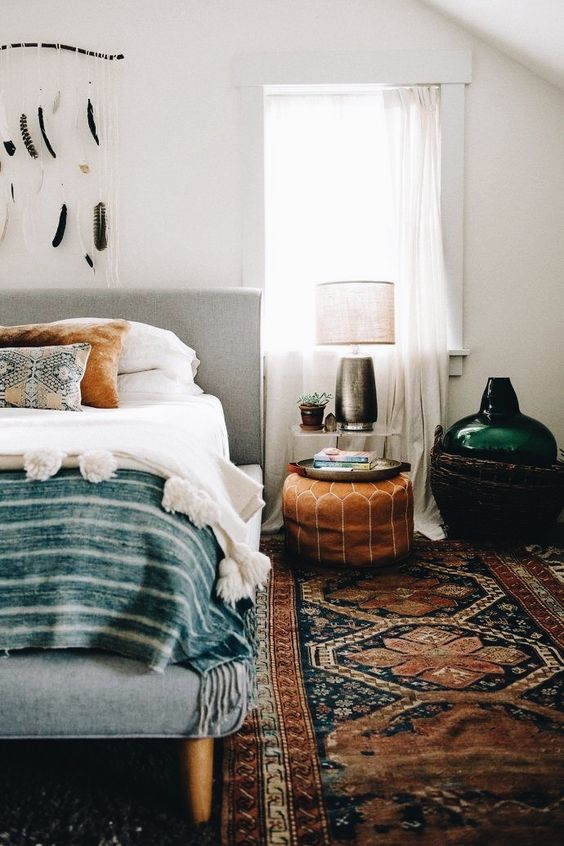 a boho rug, a leather ottoman, folksy pillows and a feather hanging for a cool boho look