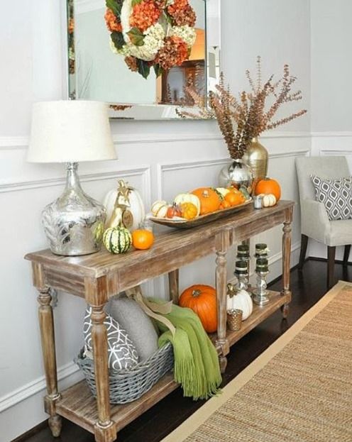a rustic console table with pumpkin arrangements, pillows, blankets and dried blooms