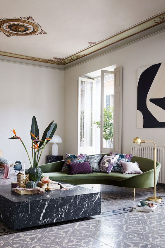 a refined curved green sofa on tall legs and a marble table are the center of the room