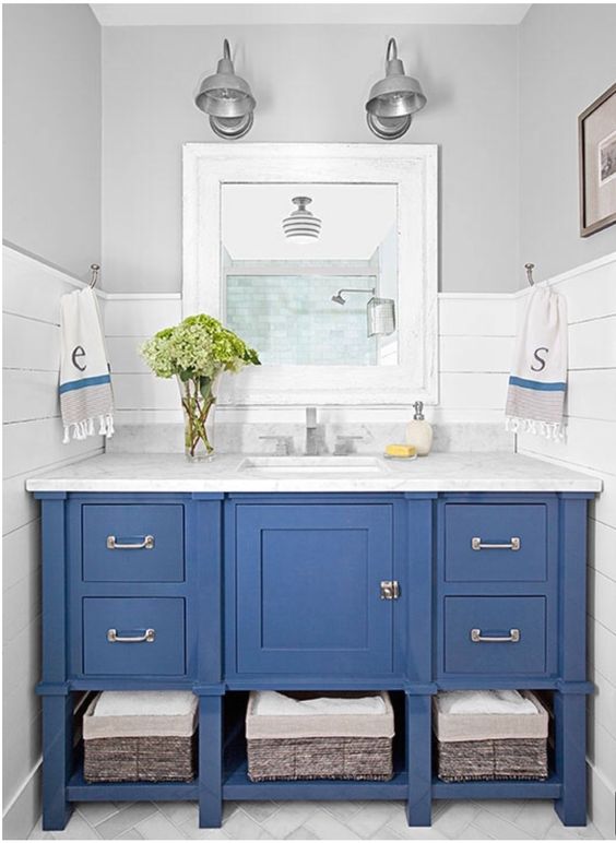 a blue vanity with baskets inside and a marble countertop for a coastal farmhouse bathroom